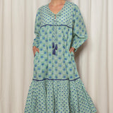 Woman wearing a green and blue patterned dress against a white curtain background