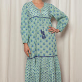 Woman wearing a green patterned dress standing against a white curtain.