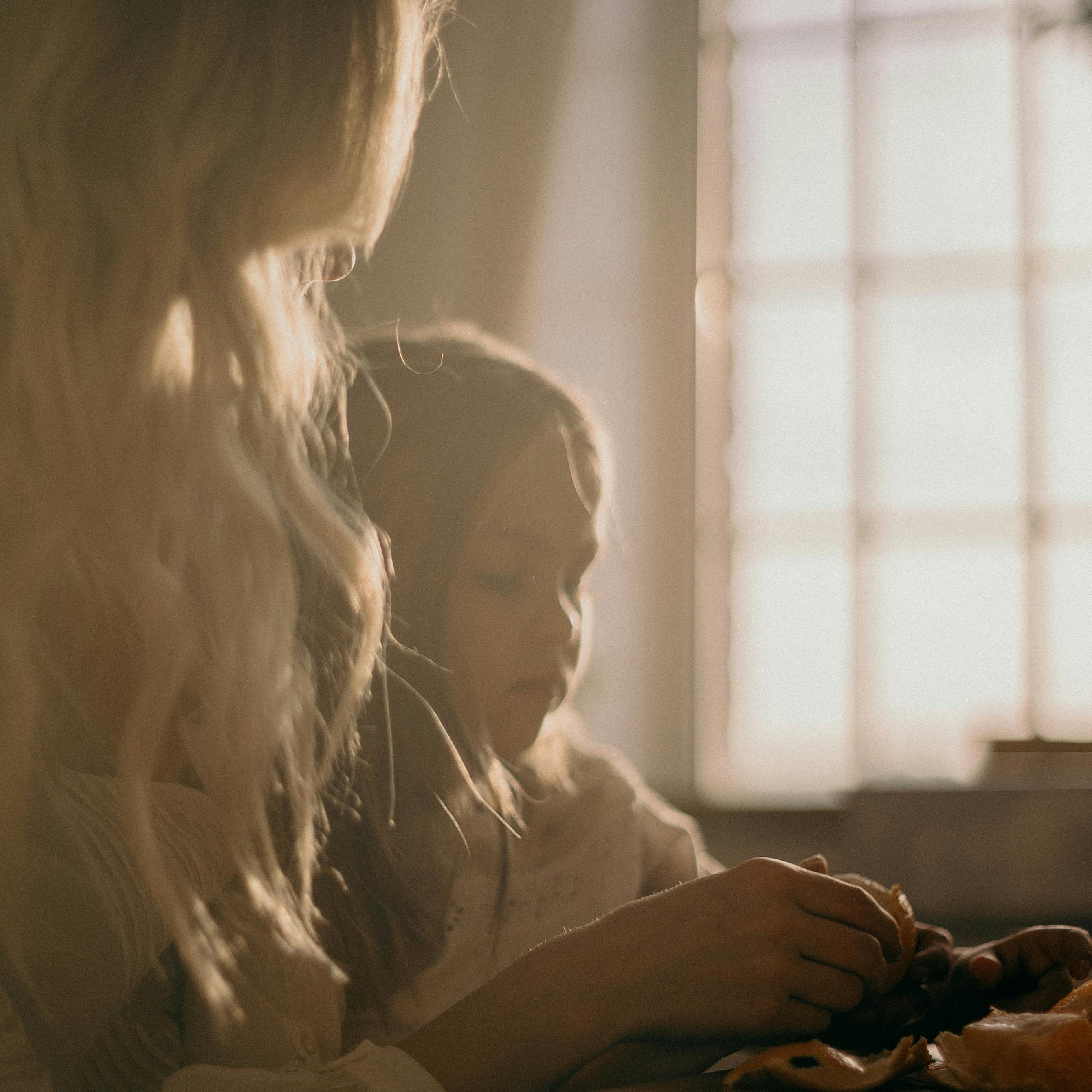 A mother and daughter sit beside a window