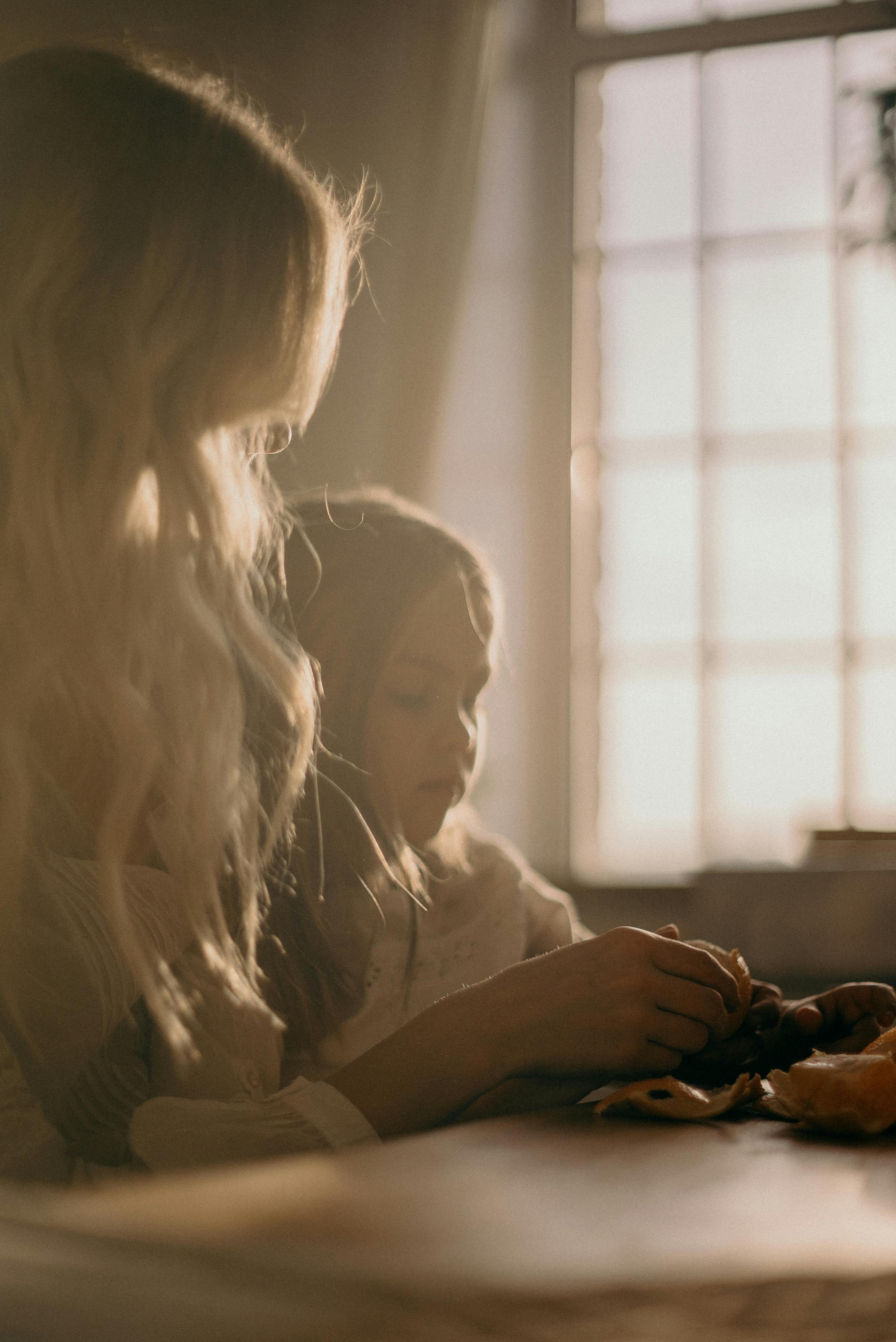 A mother and daughter sit beside a window