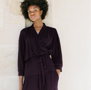 Woman wearing a dark purple outfit against a light stone wall.