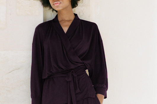 Woman wearing a dark purple outfit against a light stone wall.