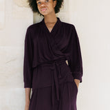 Woman wearing a dark purple outfit against a light stone wall.