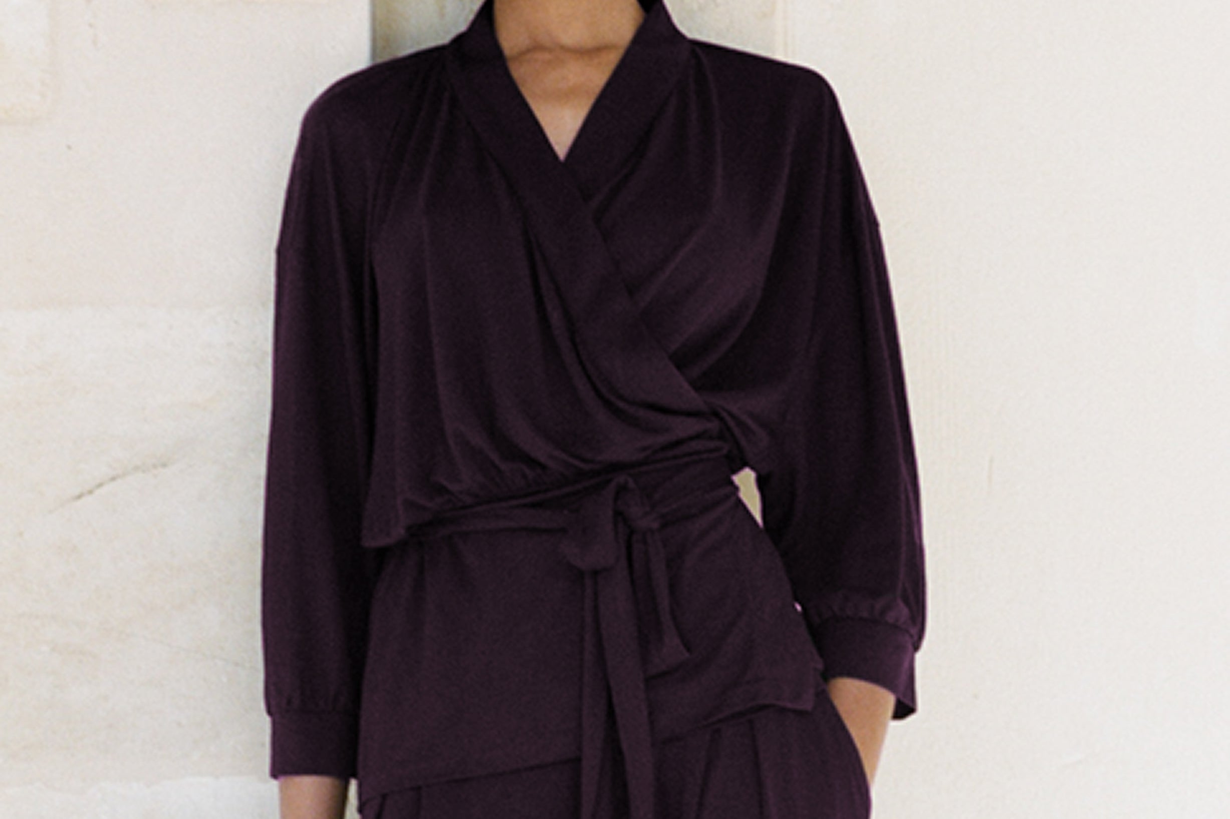 Woman wearing a dark purple outfit against a light stone wall.
