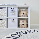Natural Tiger Belly Basket on a white shelving unit in a nursery, below a lion basket, with a patterned round rug in front