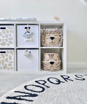 Natural Tiger Belly Basket on a white shelving unit in a nursery, below a lion basket, with a patterned round rug in front