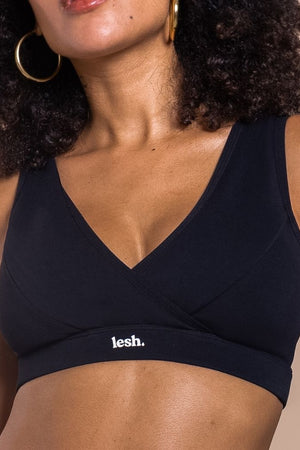 Woman wearing a black sports bra with 'lesh' branding on a beige background
