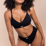 Person wearing a black bikini with 'leeh.' branding on a beige background