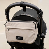 Frida Eco Stroller Organiser Taupe hanging from a black pushchair handlebar by two clips, front view
