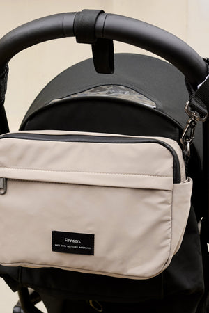 Frida Eco Stroller Organiser Taupe hanging from a black pushchair handlebar by two clips, front view