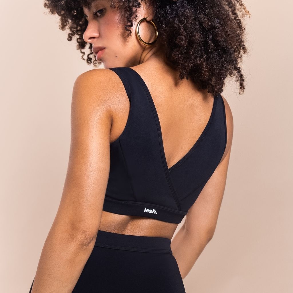 Woman wearing a black sports bra with 'lees' branding on a beige background