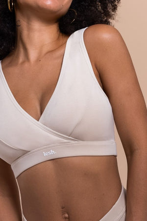 Woman wearing a beige bralette with 'fesh' branding on a beige background