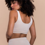 Woman wearing a white sports bra and leggings against a beige background