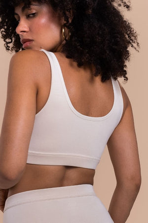 Woman wearing a white sports bra and leggings against a beige background