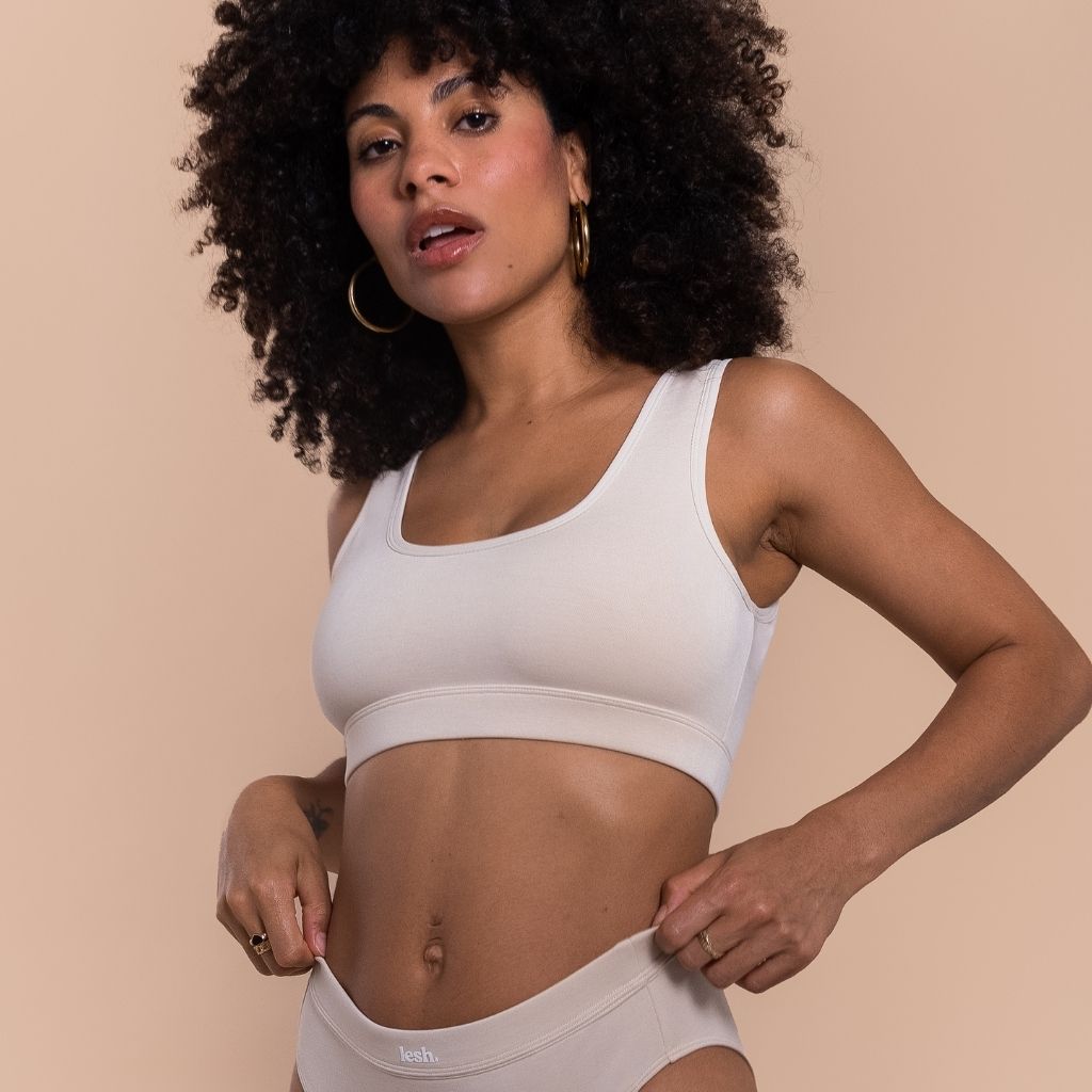 Woman wearing a white sports bra and beige underwear on a beige background
