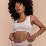 Woman wearing a white sports bra and beige underwear on a beige background