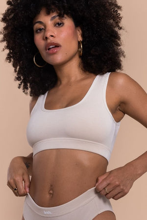 Woman wearing a white sports bra and beige underwear on a beige background