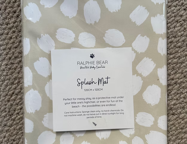 Packaged Ralphie Bear Splash Mat with white abstract pattern on a beige background