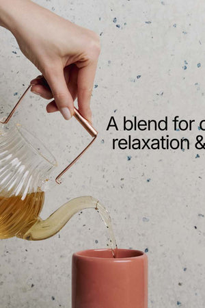 Tea being poured from a glass teapot into a pink cup with text 'A blend for deep relaxation & rest' on a speckled surface.