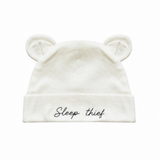 An off-white baby beanie hat with embroidered bear ears on top and the phrase 'Sleep thief' embroidered in black script on the front cuff, shown against a plain white background.