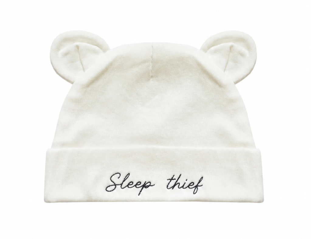 An off-white baby beanie hat with embroidered bear ears on top and the phrase 'Sleep thief' embroidered in black script on the front cuff, shown against a plain white background.