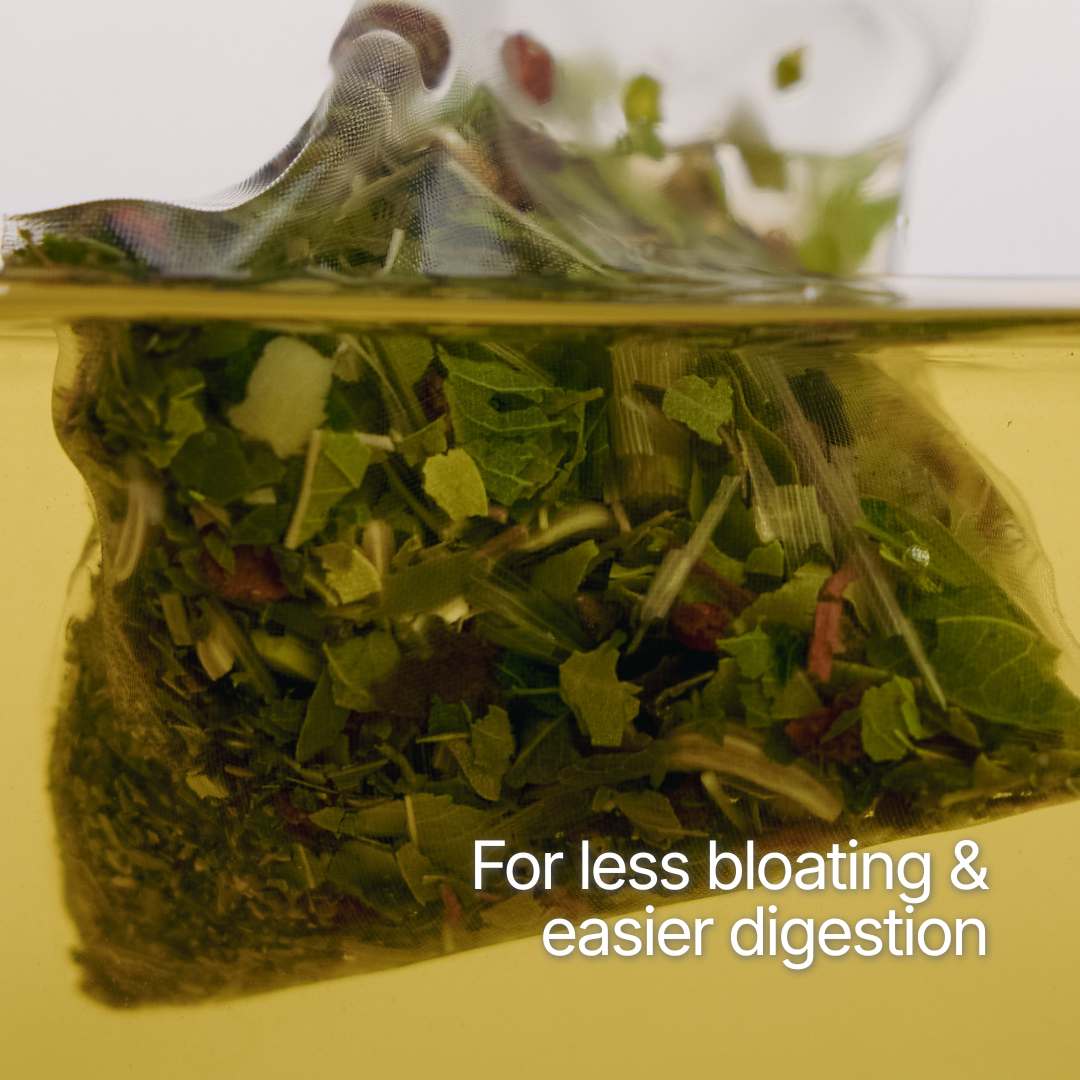A clear tea bag filled with green tea leaves and herbs, partially submerged in yellow liquid with white text reading 'For less bloating & easier digestion'.