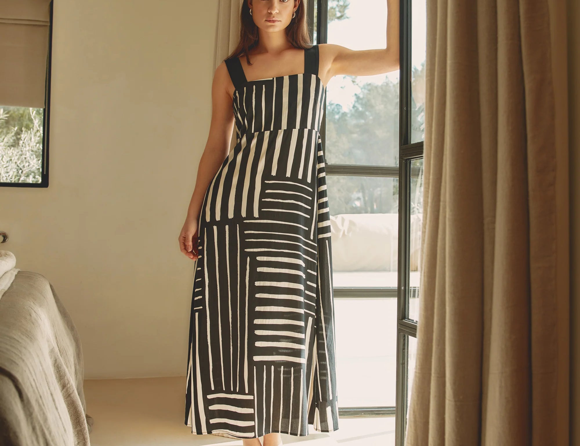 Woman in a black and white striped dress standing in a room with a large window.