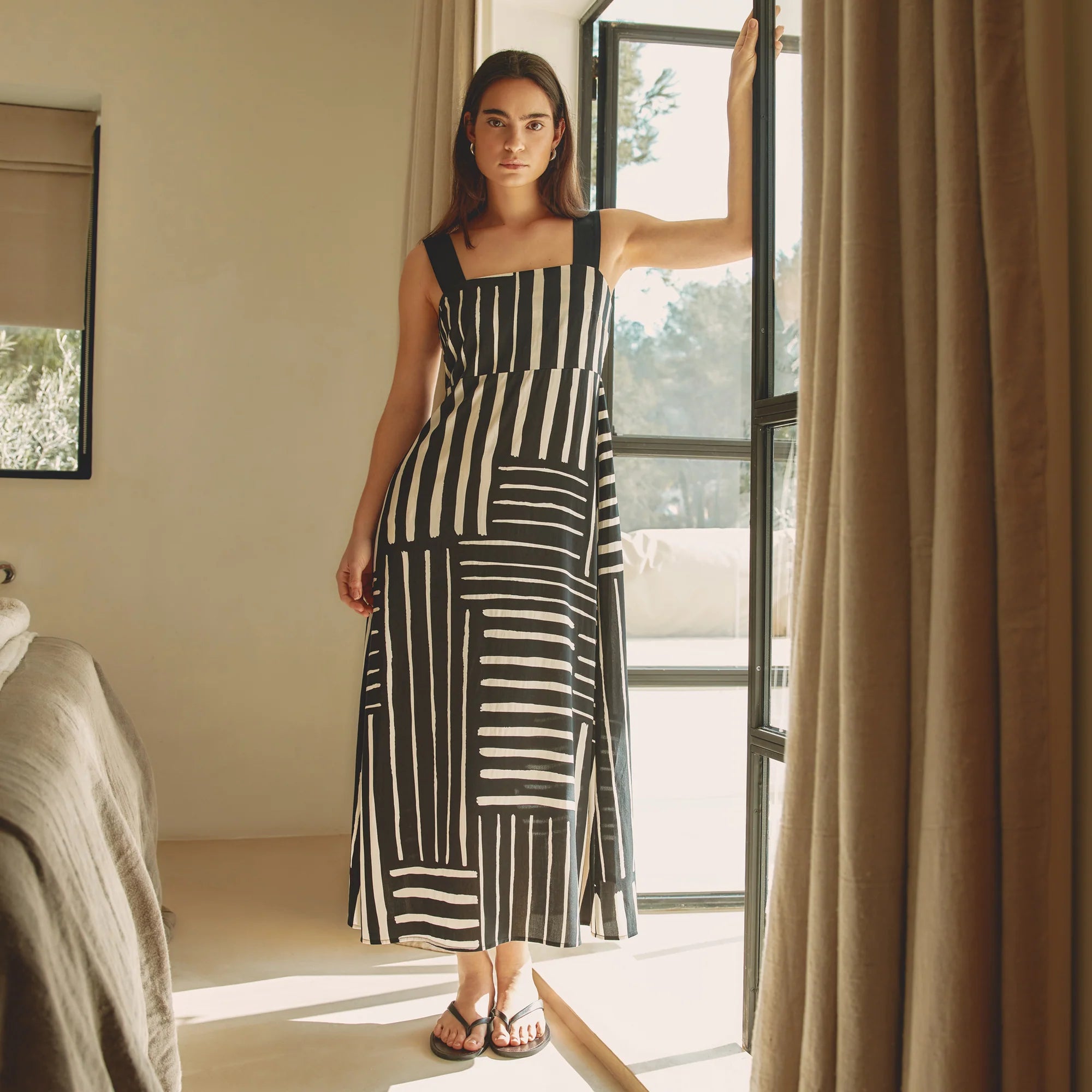 Woman in a black and white striped dress standing in a room with a large window.