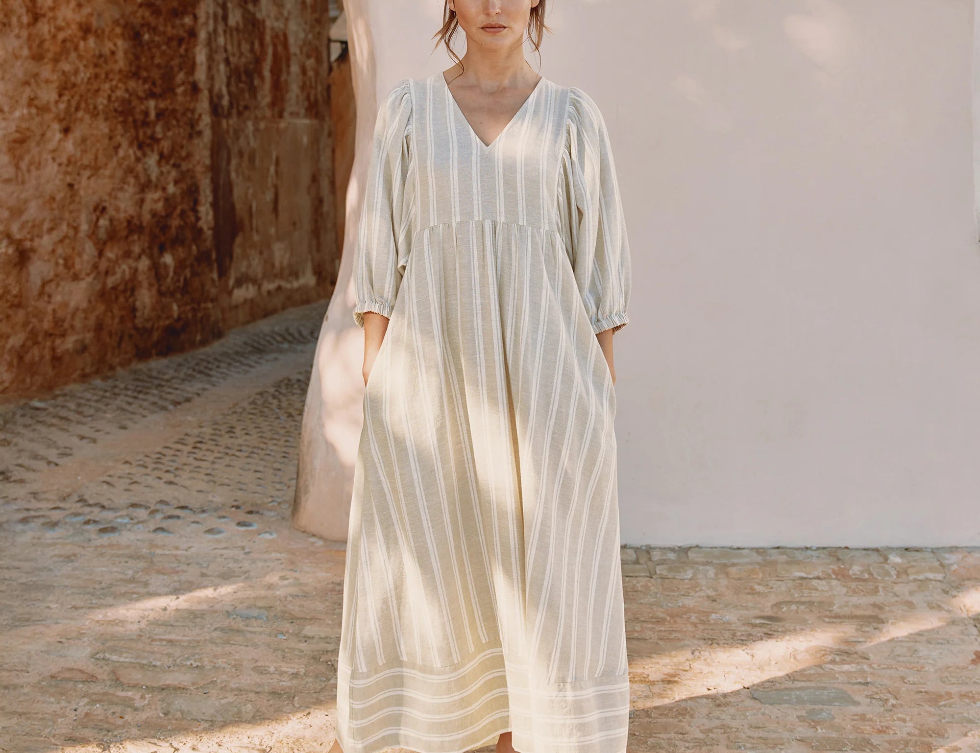 Woman wearing a light-colored dress standing in a sunlit outdoor setting.