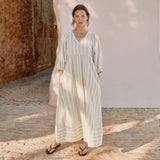 Woman wearing a light-colored dress standing in a sunlit outdoor setting.