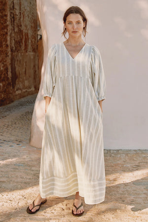 Woman wearing a light-colored dress standing in a sunlit outdoor setting.