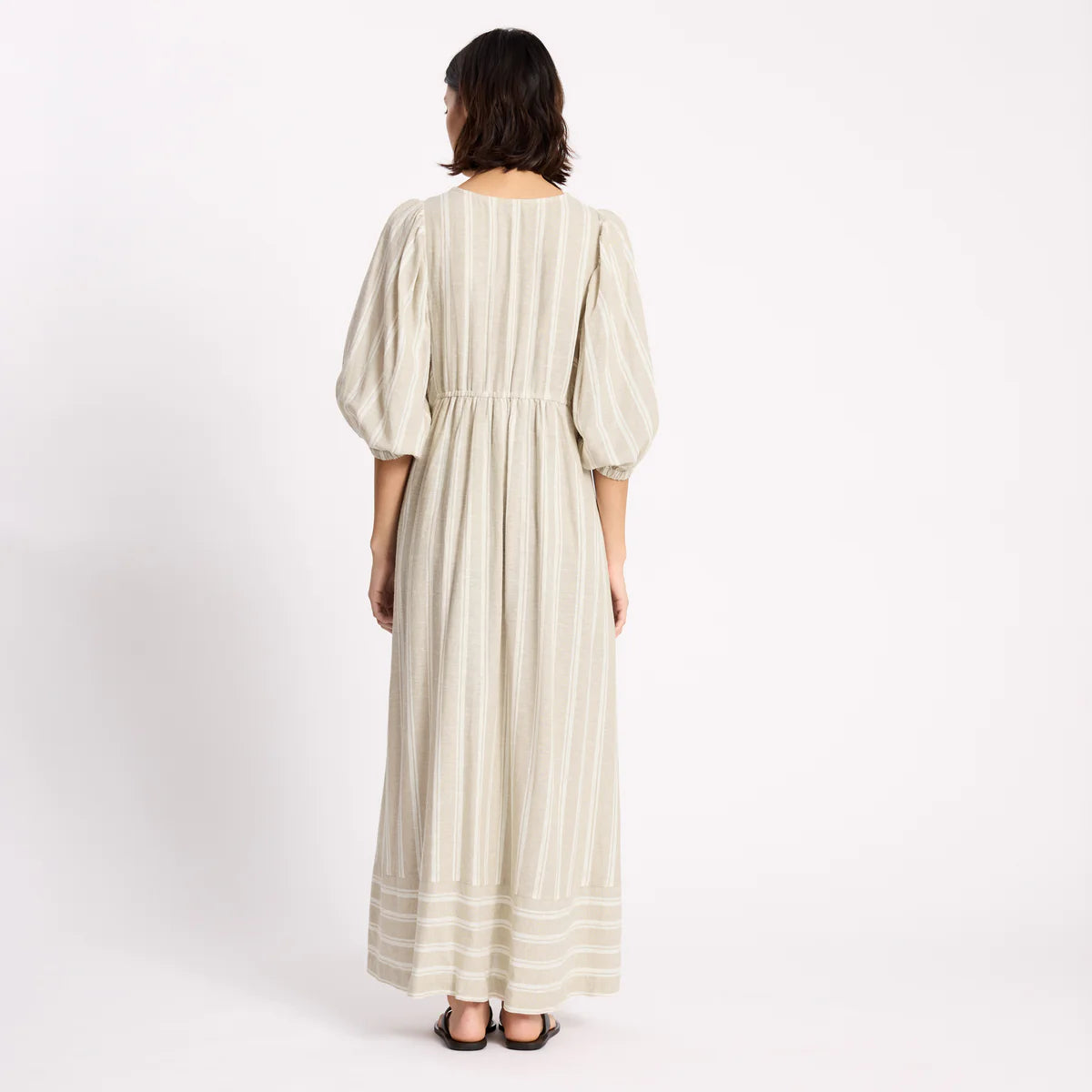 Woman wearing a long, light-colored dress with puffed sleeves on a white background