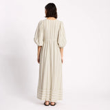 Woman wearing a long, light-colored dress with puffed sleeves on a white background