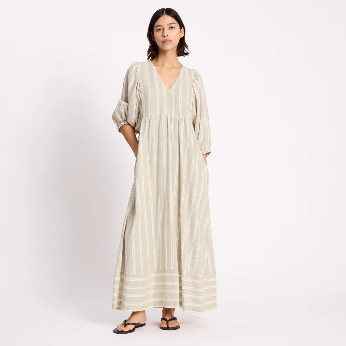 Woman wearing a long, light-colored dress with stripes on a white background
