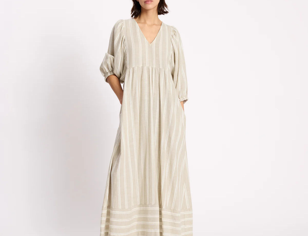 Woman wearing a long, light-colored dress with stripes on a white background