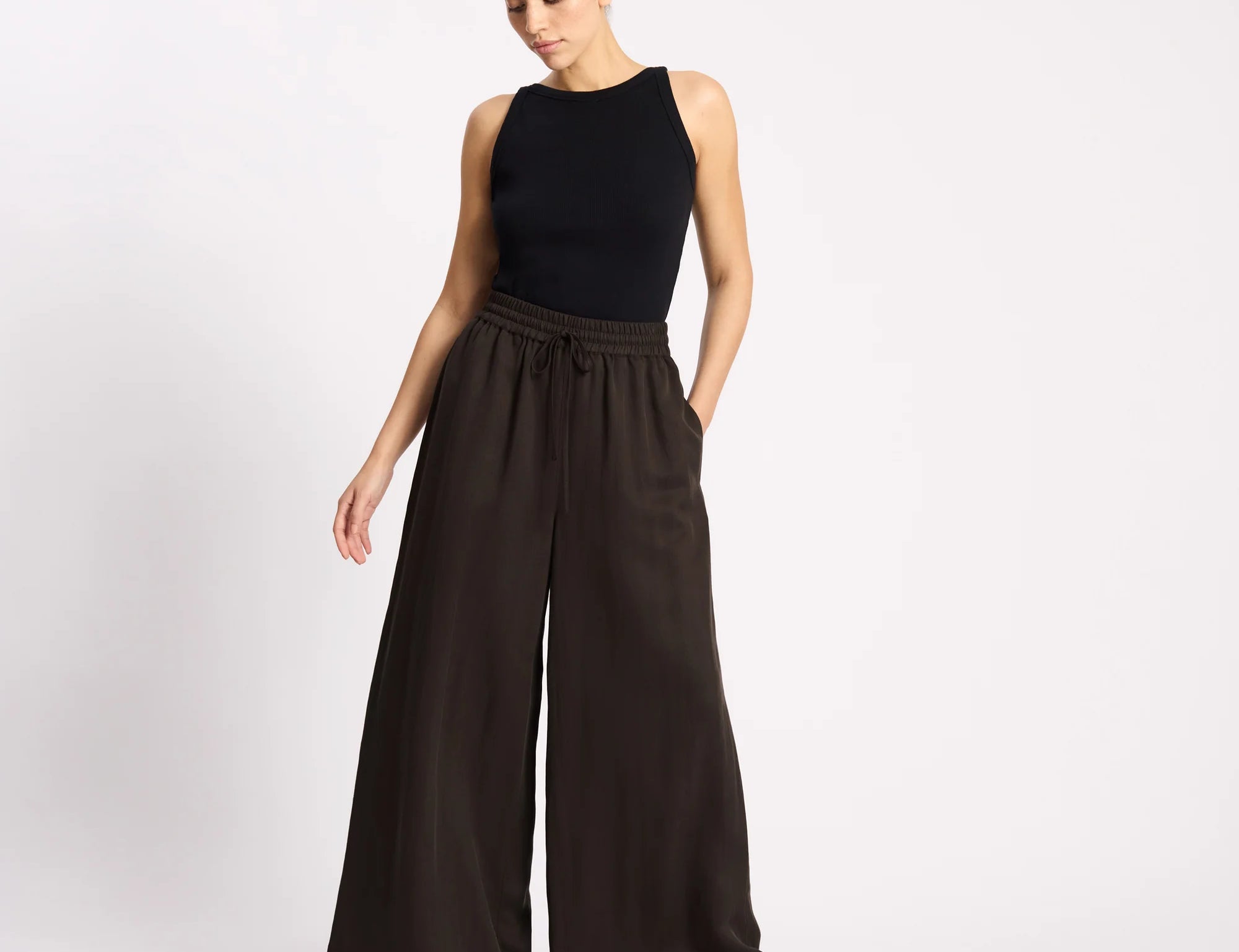 Woman wearing a black sleeveless top and wide-leg pants on a white background