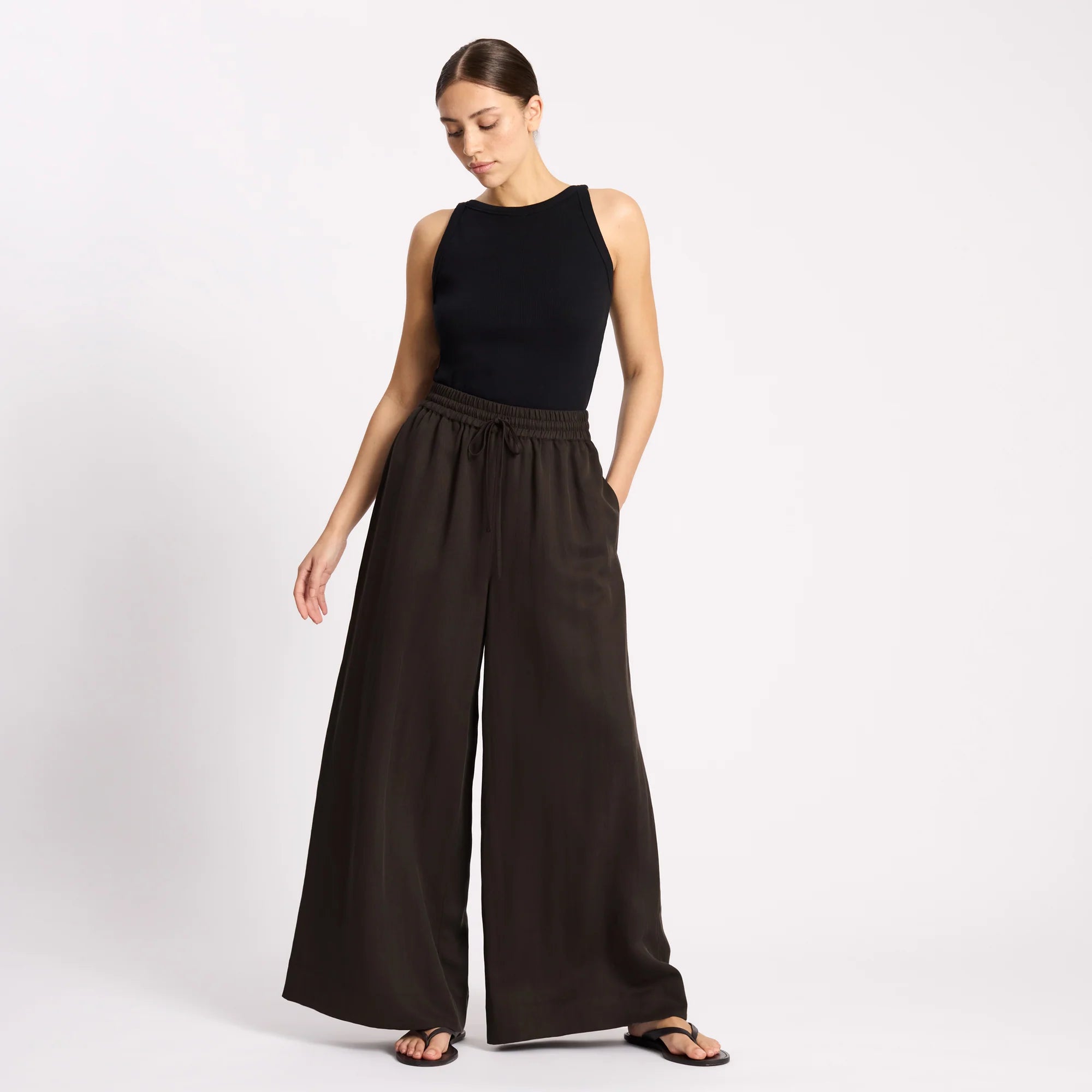 Woman wearing a black sleeveless top and wide-leg pants on a white background