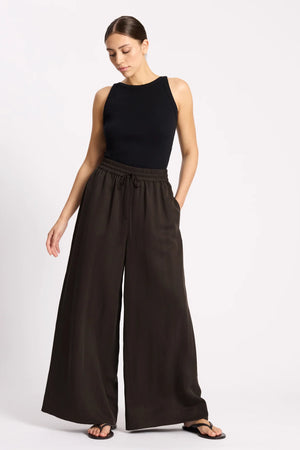 Woman wearing a black sleeveless top and wide-leg pants on a white background