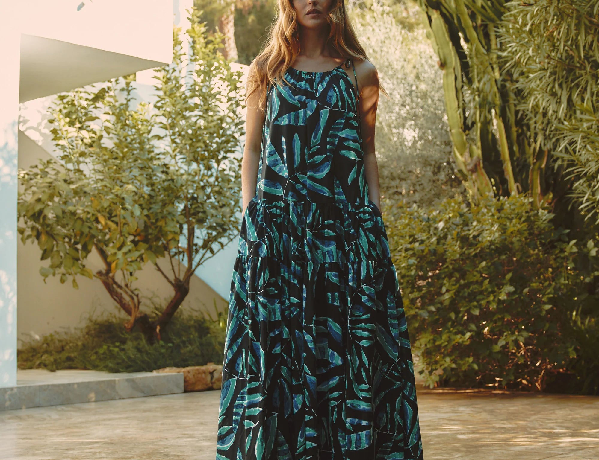 Woman in a blue and black patterned dress standing outdoors with greenery in the background