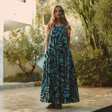 Woman in a blue and black patterned dress standing outdoors with greenery in the background
