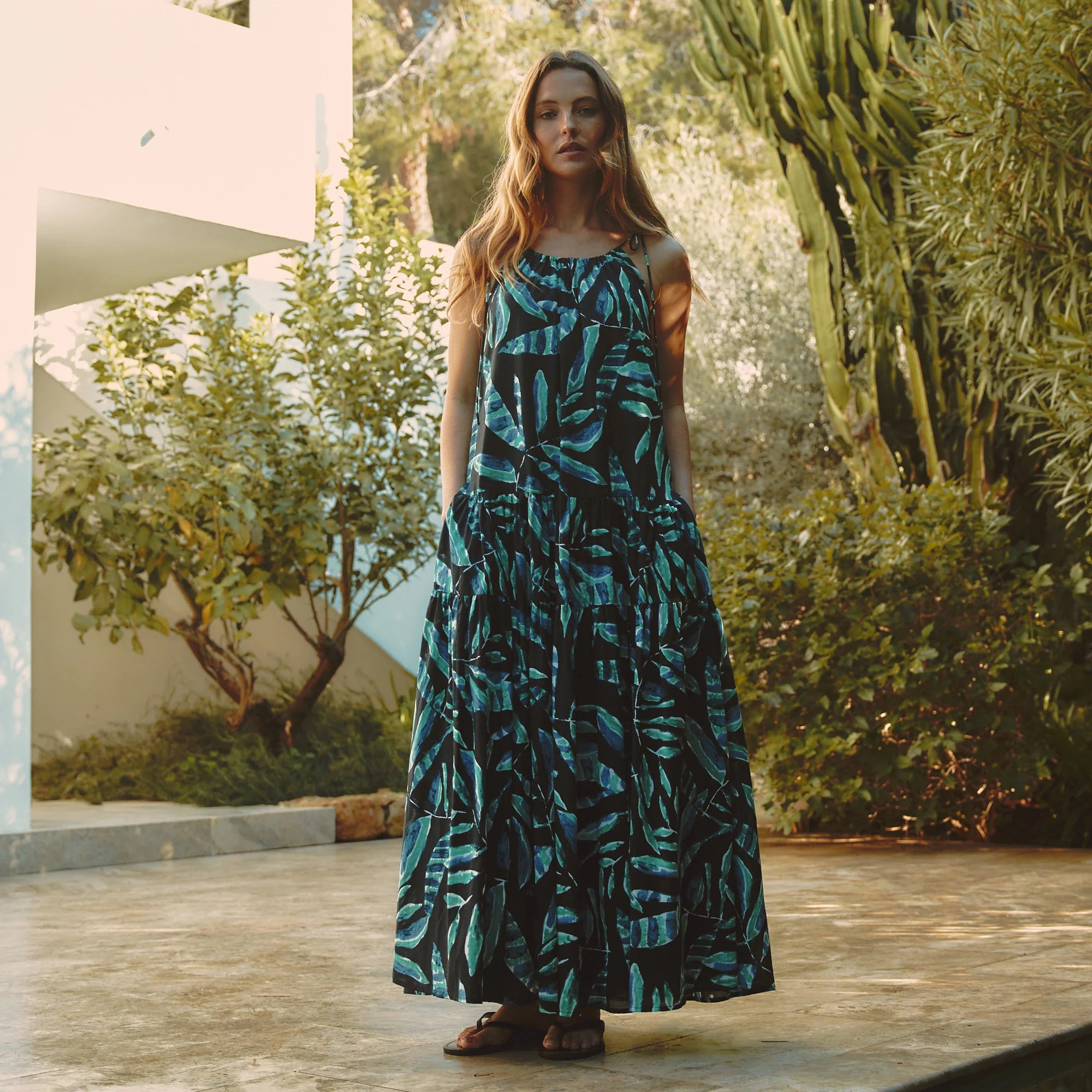 Woman in a blue and black patterned dress standing outdoors with greenery in the background