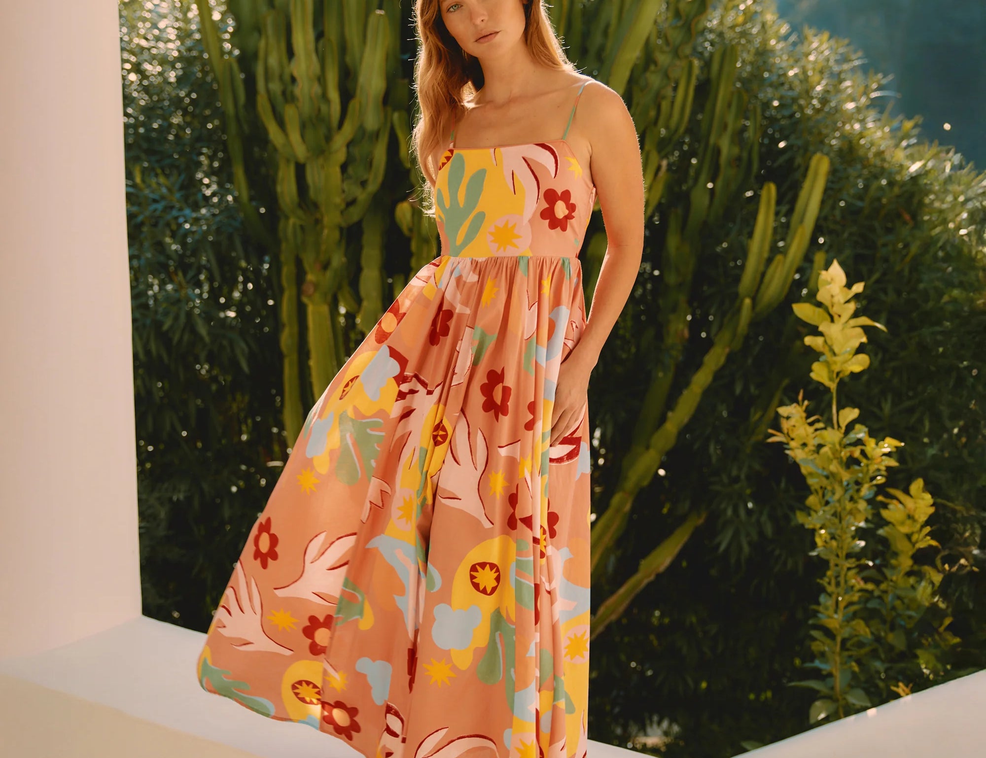 Woman in a colorful floral dress standing outdoors with greenery in the background