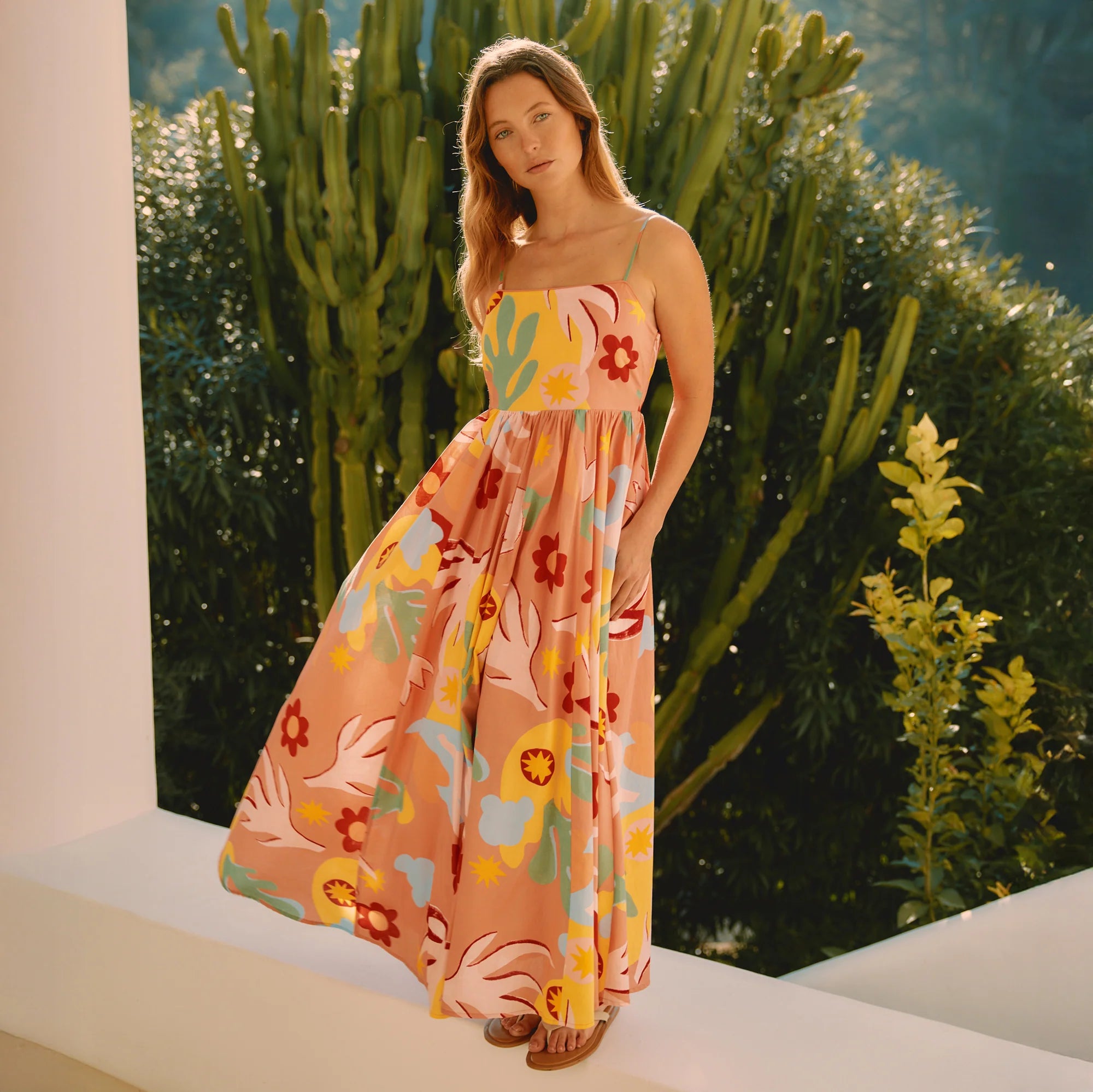 Woman in a colorful floral dress standing outdoors with greenery in the background
