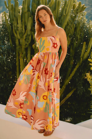 Woman in a colorful floral dress standing outdoors with greenery in the background