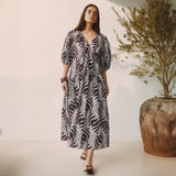Woman wearing a patterned dress standing next to a potted plant indoors.