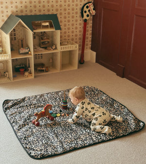 Thoren Eco Playmat in Leopard laid on a bedroom carpet with a baby crawling towards wooden toys