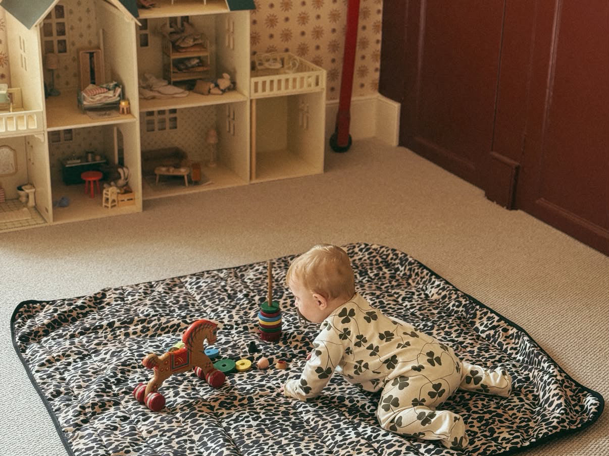 Thoren Eco Playmat in Leopard laid on a bedroom carpet with a baby crawling towards wooden toys