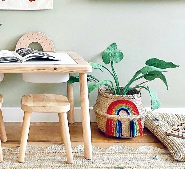 Vivid Rainbow Belly Basket holding a green plant, next to a wooden children's table and stool