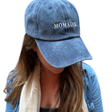 A person wearing a blue denim baseball cap with the word 'MOMAGER' embroidered in white on the front, shown against a plain white background.