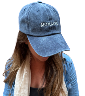 A person wearing a blue denim baseball cap with the word 'MOMAGER' embroidered in white on the front, shown against a plain white background.
